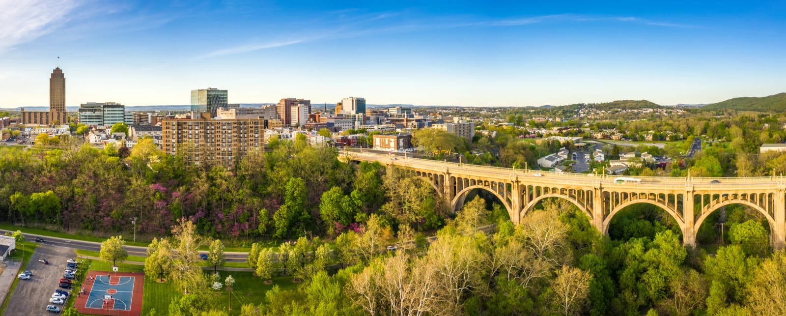 City skyline and an arched bridge above a tree-lined park in the Lehigh Valley.